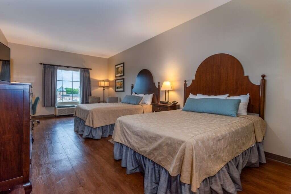 Hotel room with two double beds, wooden headboards, beige bedding, and blue accents.