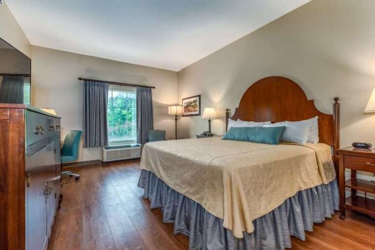 Bedroom with a large wooden bed, wooden dresser, blue chair, and window with gray curtains.