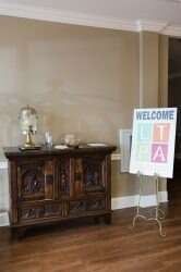 A wooden cabinet with a lamp, next to a welcome sign in a room.