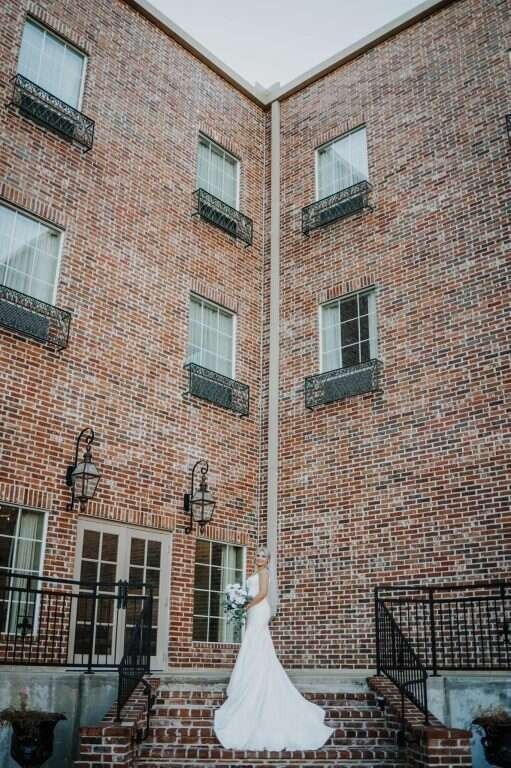Bride in white dress poses on brick steps outside a building.