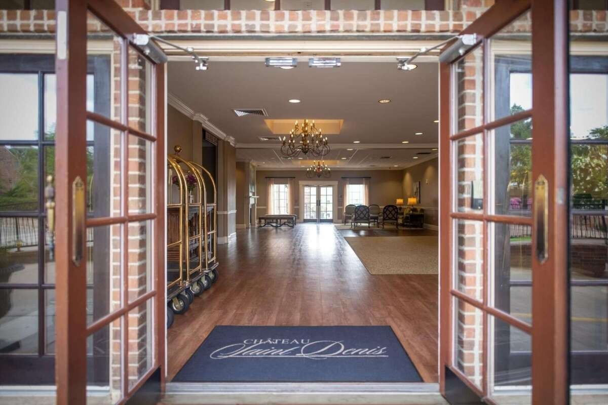 Entrance to Chateau du Dome hotel: open doors reveal lobby with luggage cart, wood floors, and chandelier.