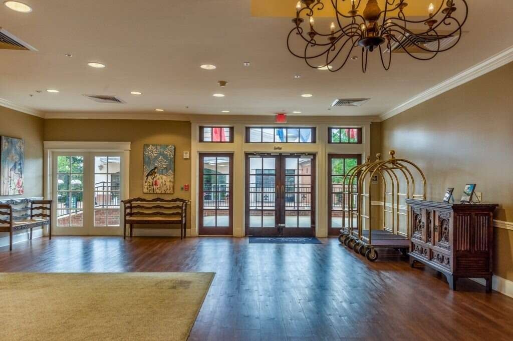 Hotel lobby with dark wood floors, wooden furniture, and glass doors leading outside.