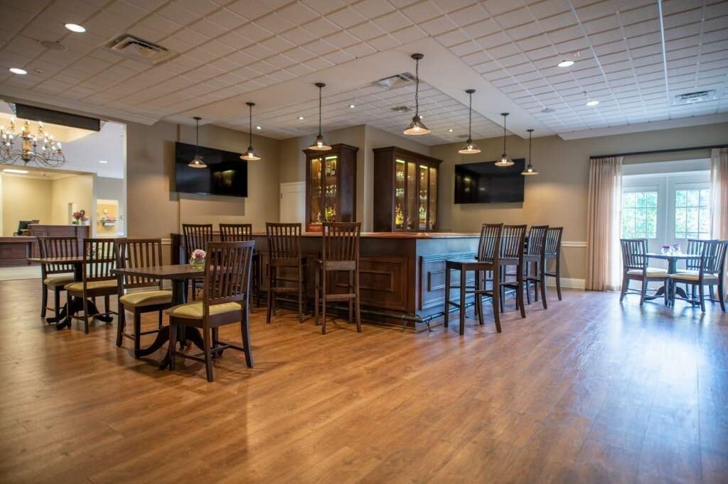 Interior bar with wooden floors, bar stools, tables, and display cabinets.