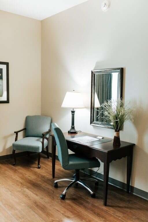 Desk with a chair, lamp, mirror and chair in a room with wood-look flooring and neutral walls.