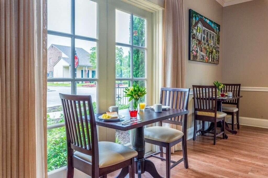 Breakfast table near a window. Two chairs face the table set with food, coffee, and a flower vase.