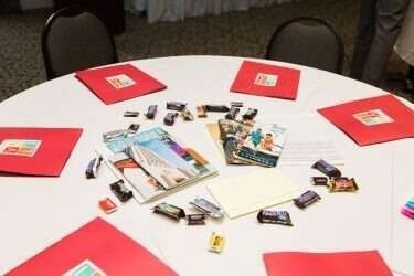 A white table with red folders, brochures, and small items scattered on it.