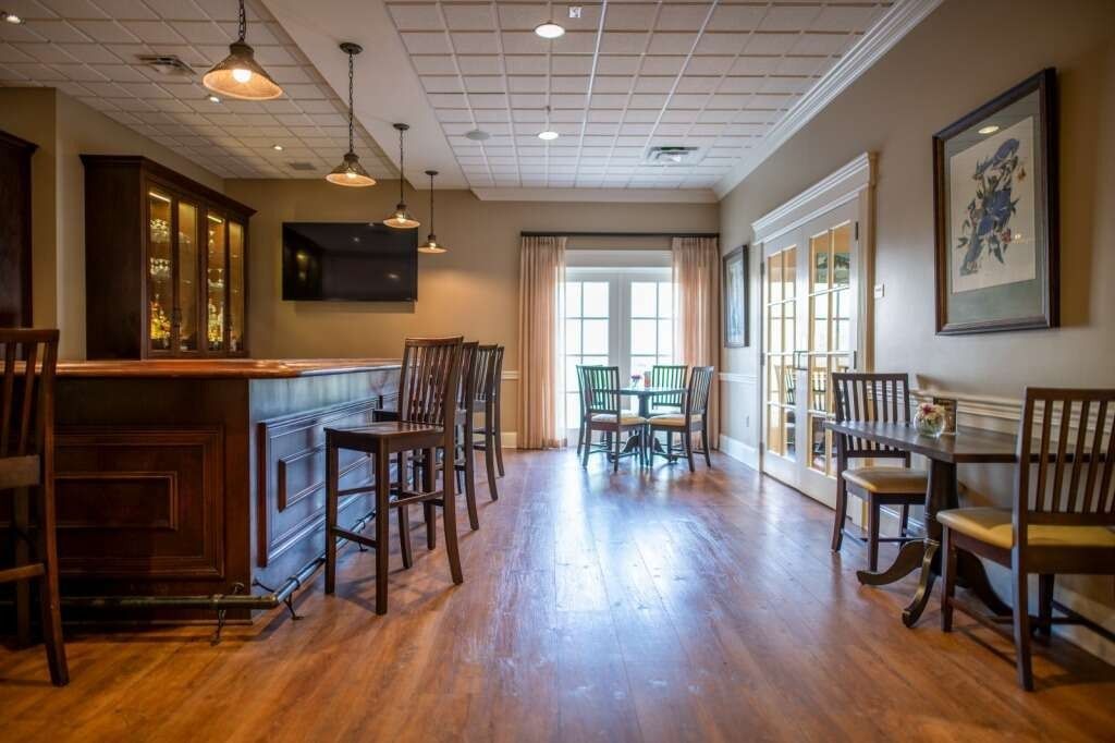 Interior of a bar with a wooden counter, stools, and tables. Window at the end of the room.
