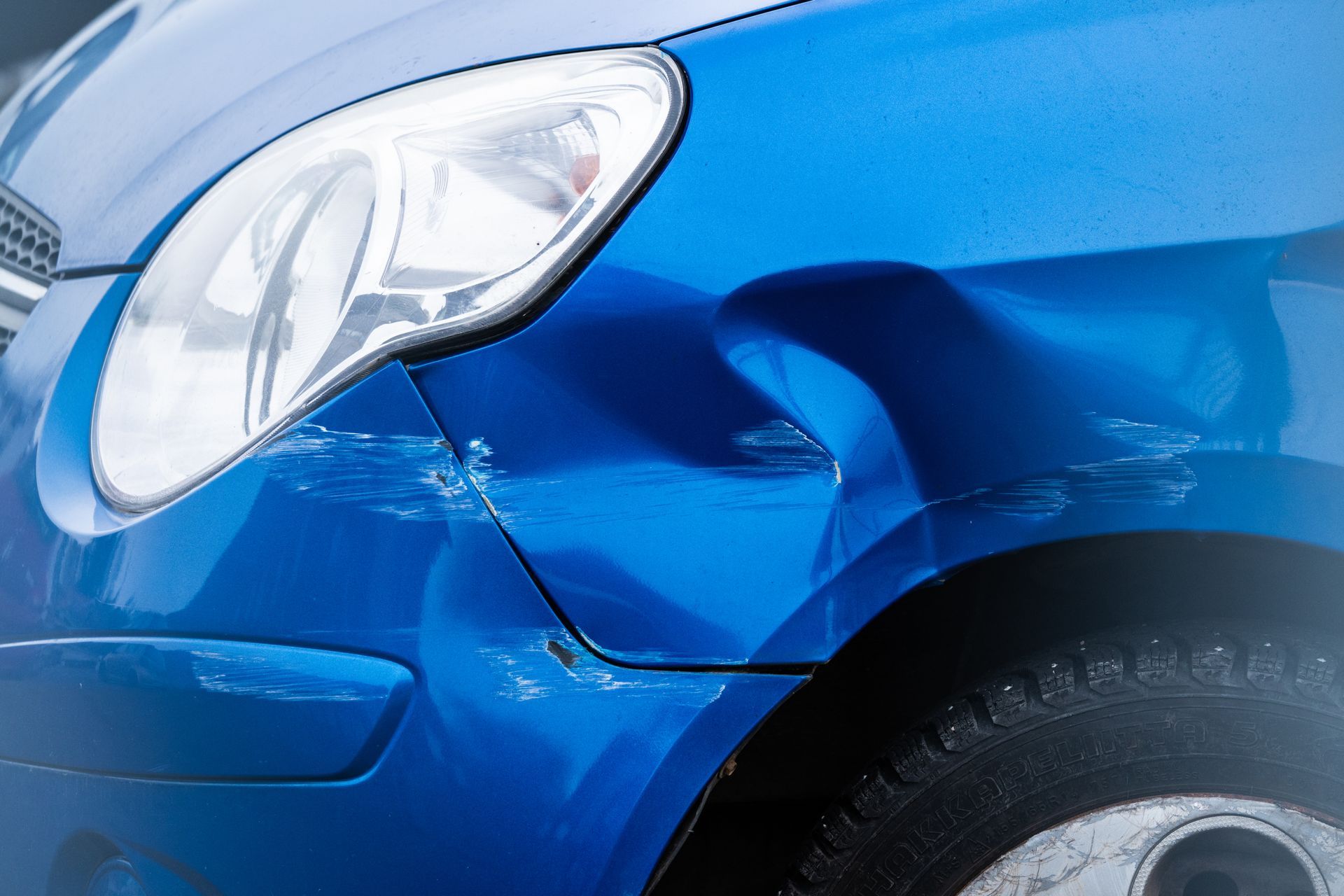 Blue car with scratched and dented front fender panel.