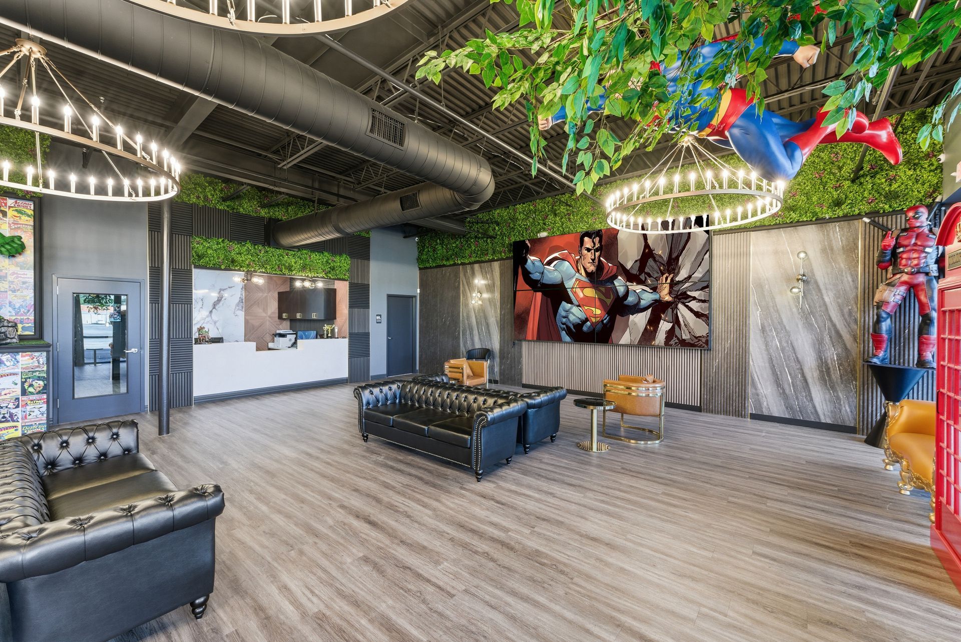 Reception area with superhero theme. Black leather sofas, art, green foliage, and chandelier lights.