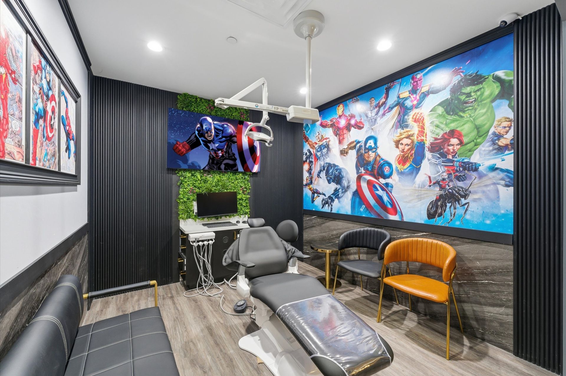 Dental room with superhero-themed decor, including artwork, a screen playing Captain America, and a dental chair.