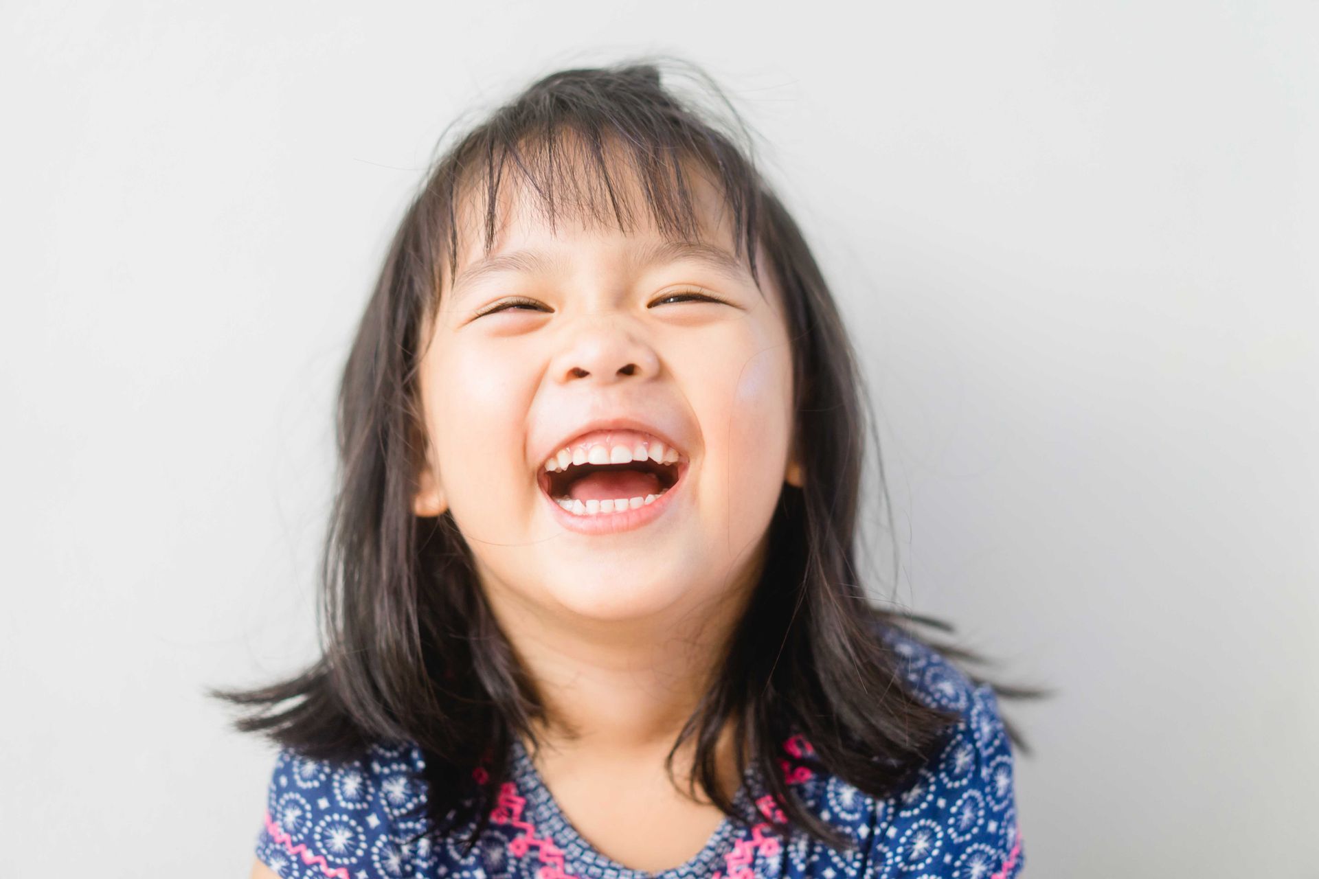 Smiling child with dark hair and bangs, laughing with mouth open.
