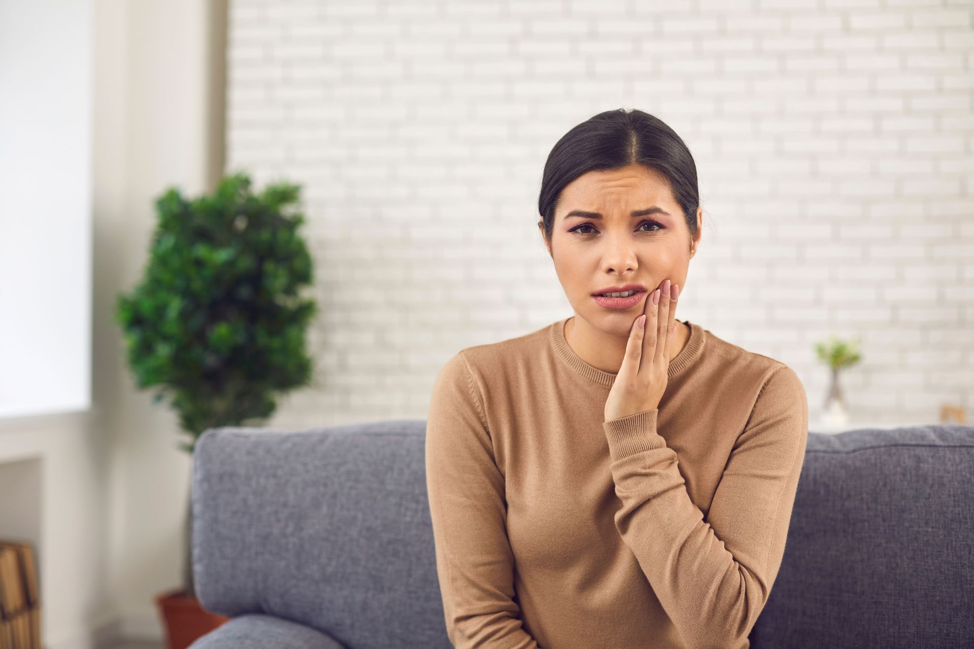 Woman on a couch holding her cheek, appearing to be in pain.
