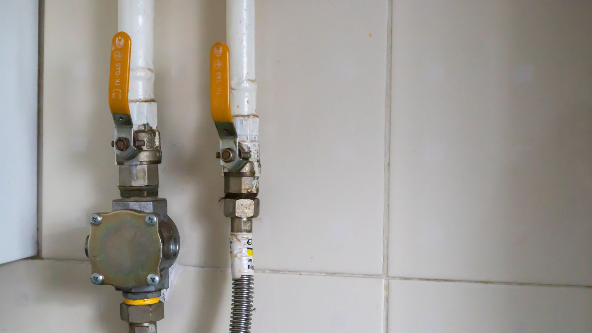 A person in a blue shirt uses a wrench to repair the metal pipes underneath a kitchen sink.