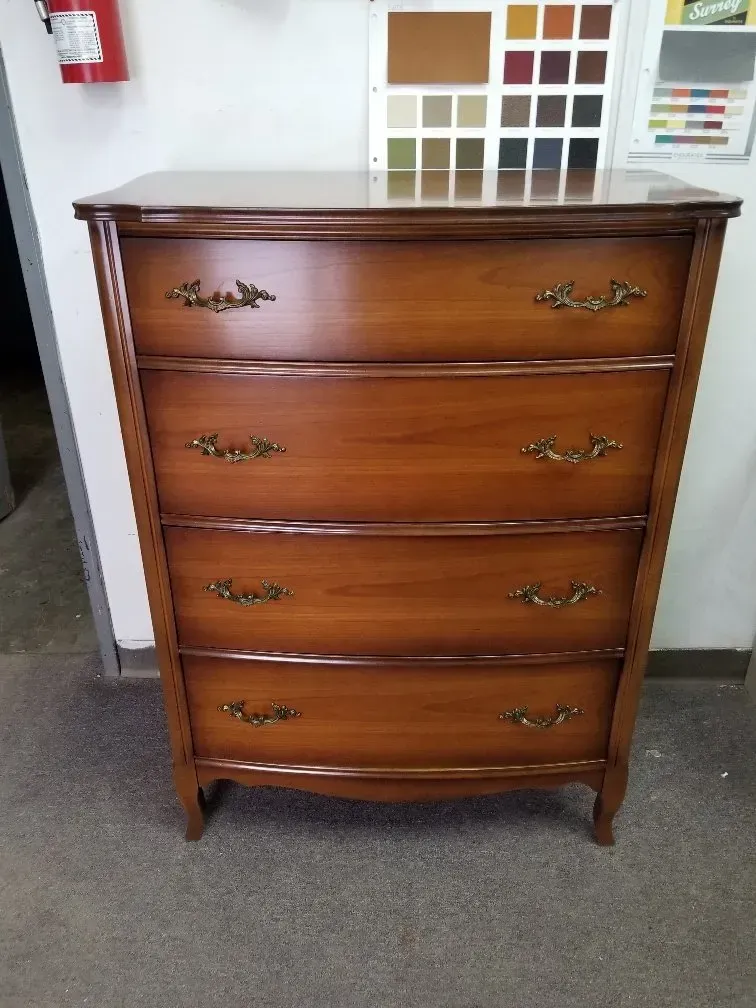 A brown wooden dresser with four drawers, each featuring two ornate brass-colored handles, set against a white wall.