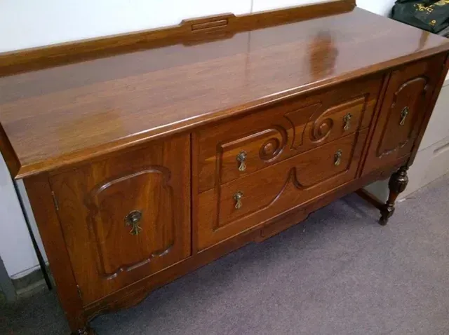 A polished wooden sideboard featuring a long flat top, two side cabinets, and a central section with drawers and carving.