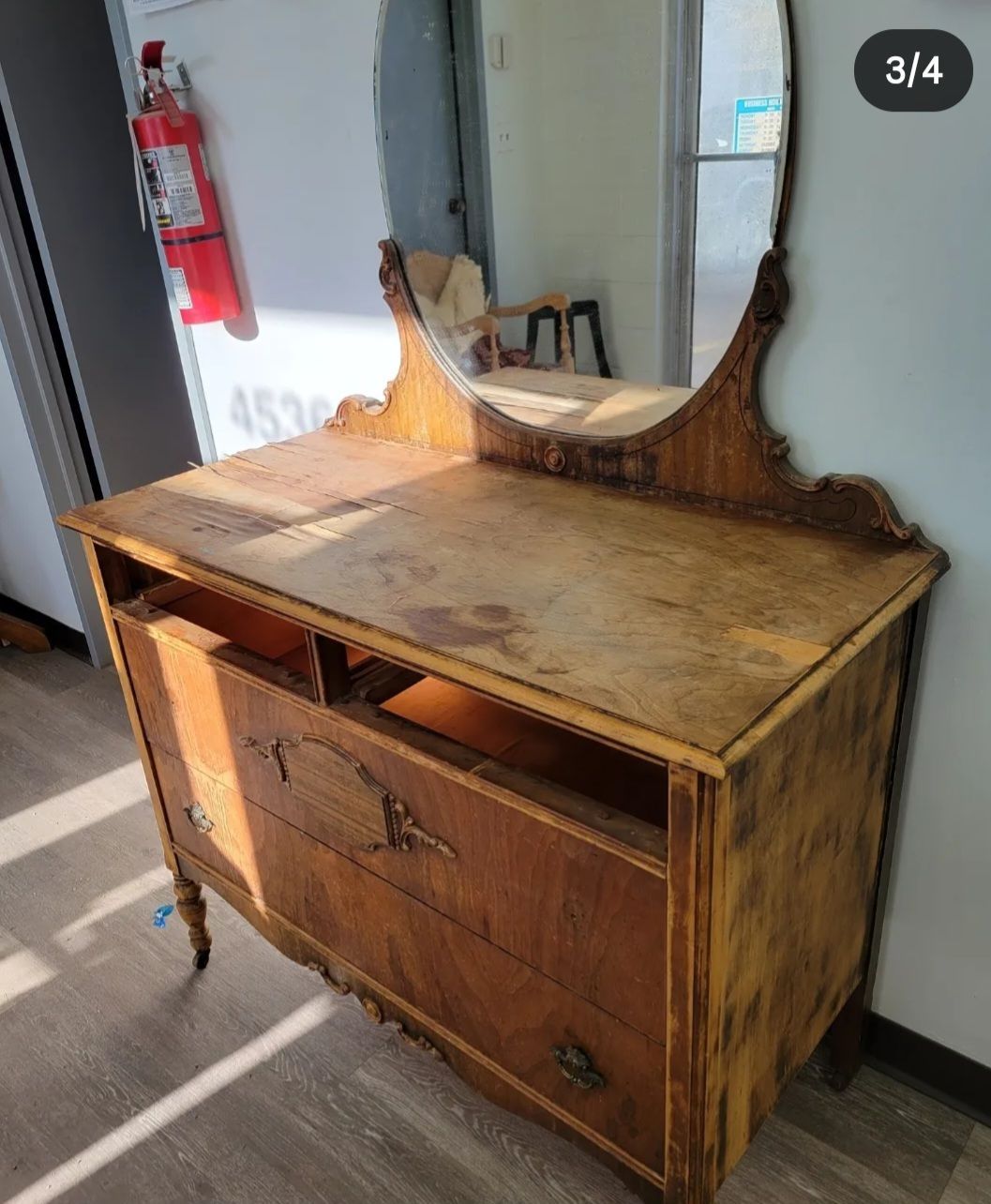 A weathered, wooden two-tiered side table with spindled legs and a missing piece of veneer on the front cabinet door.