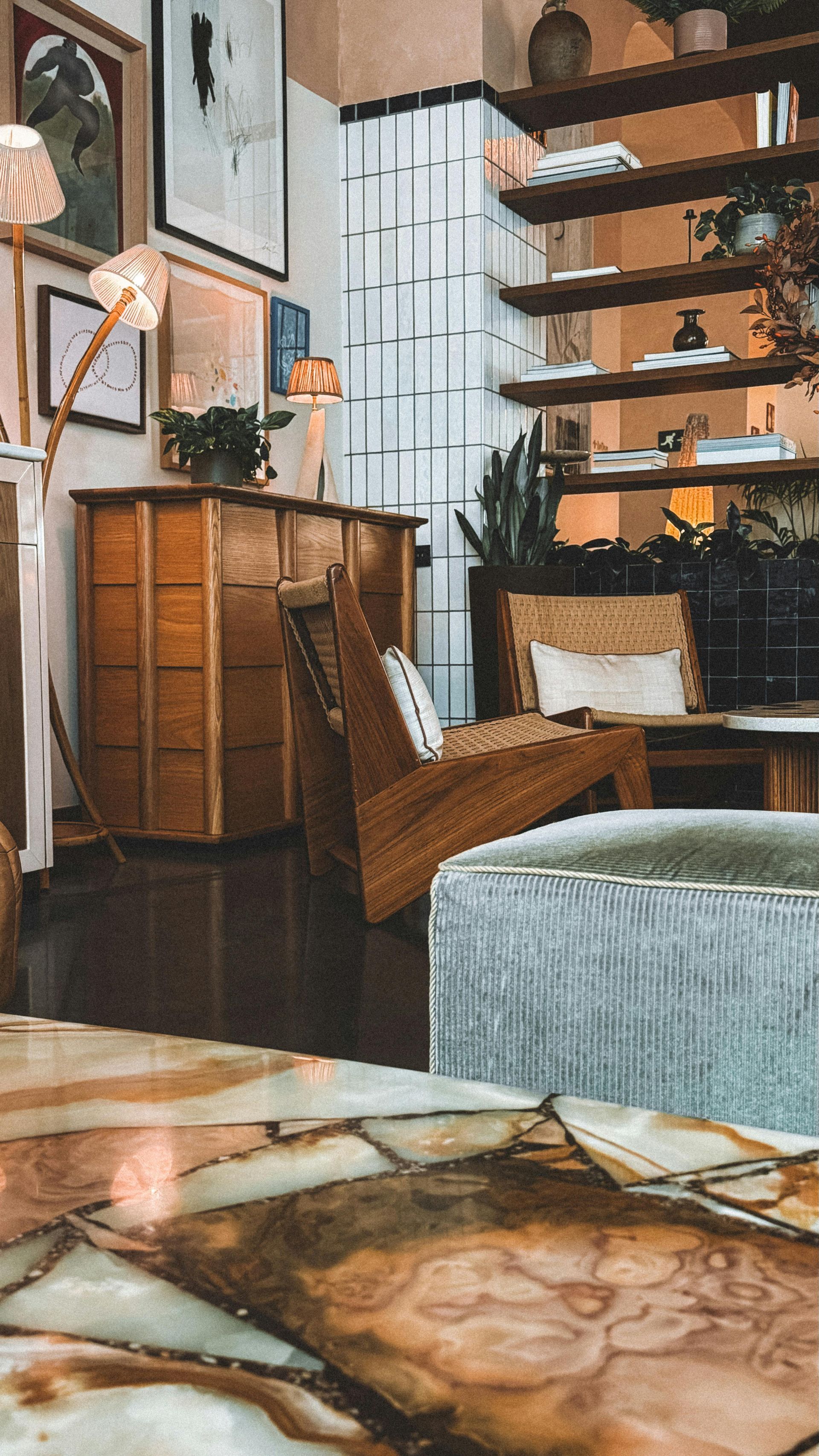 A room interior featuring a large stone coffee table, a wooden lounge chair, shelving, and decor in a warm-toned space.