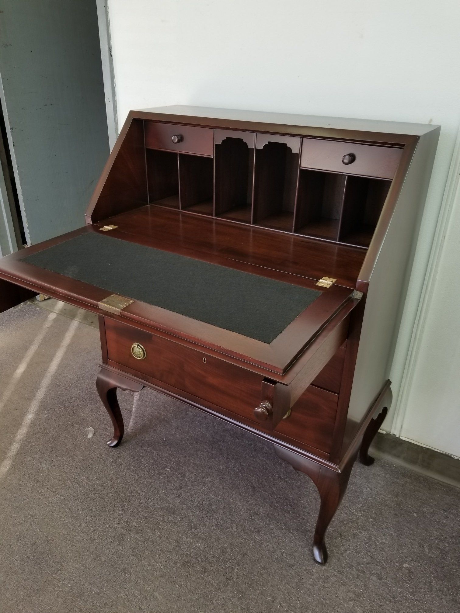 Wooden roll-top secretary desk with drawers and open writing surface in a room.