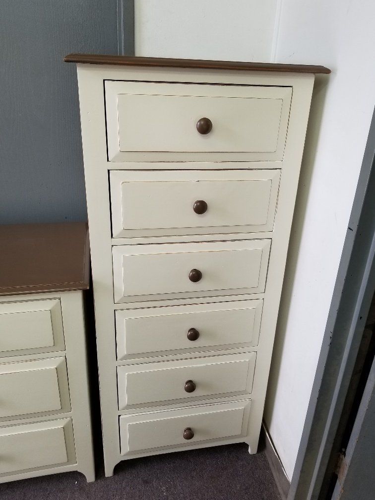 Tall cream dresser with six drawers and brown top beside a smaller white chest in a room.