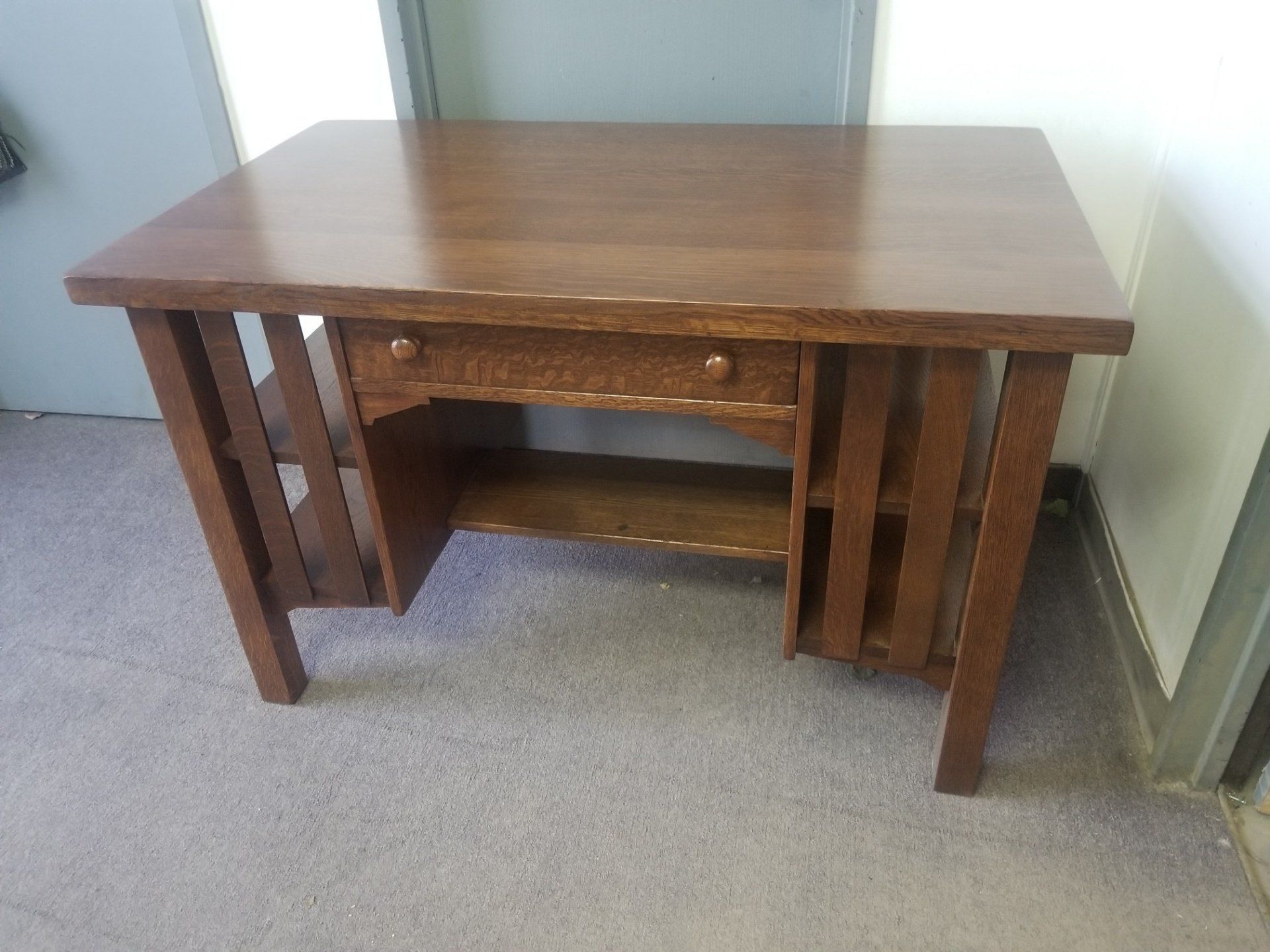 Small wooden desk with a center drawer in a carpeted room, against a wall.