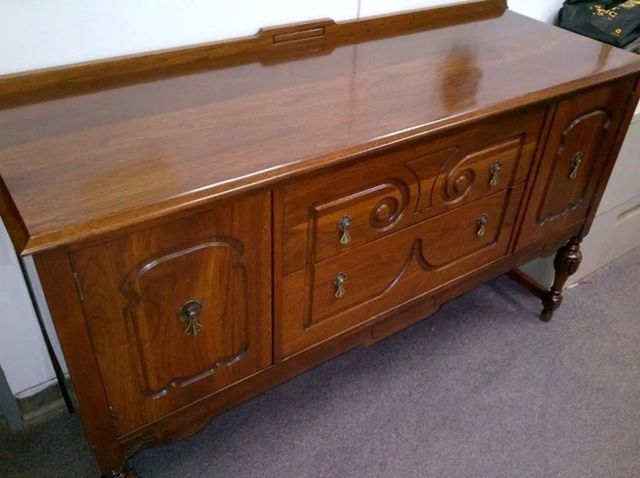 Wooden antique sideboard cabinet with ornate carved details on a carpeted floor.