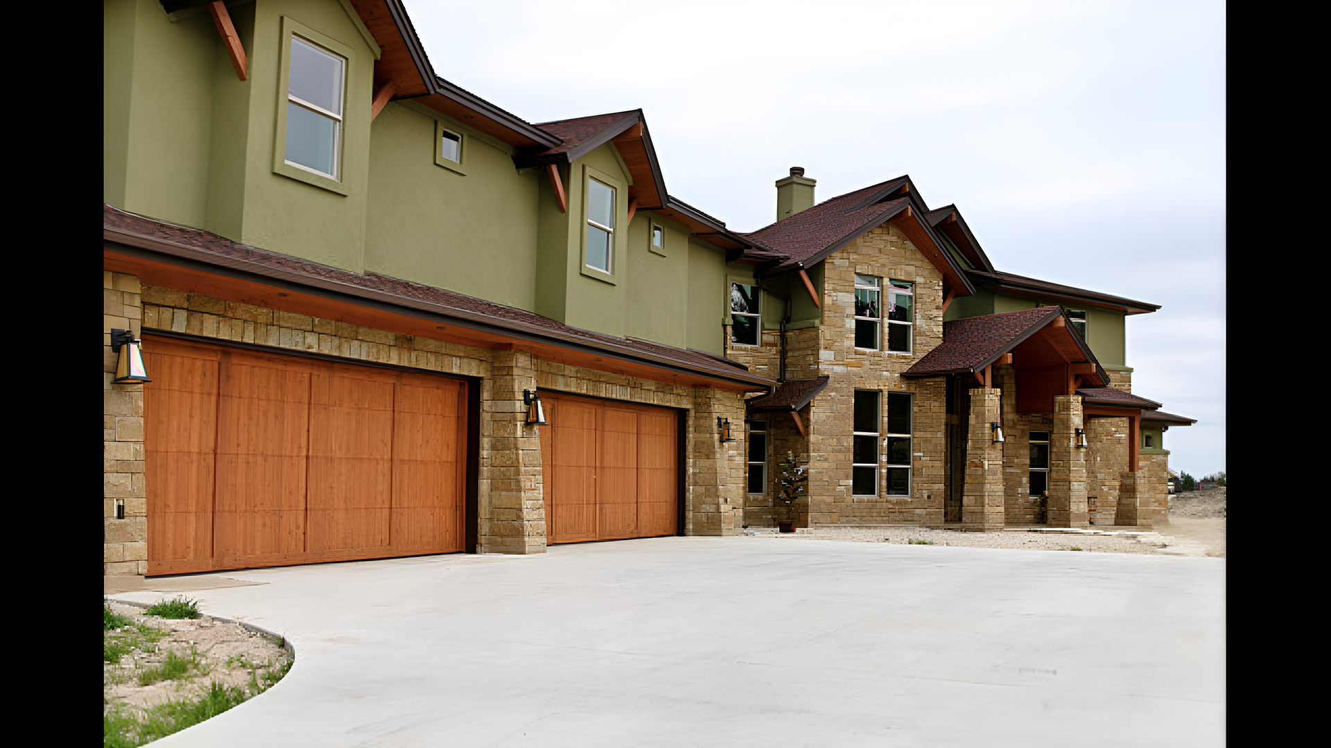 Large stone and stucco suburban house with three wooden garage doors and a snowy driveway