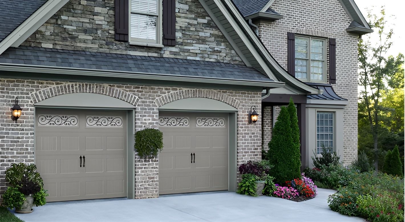 Elegant stone house front with two beige garage doors, manicured shrubs, and pink flowers by the driveway