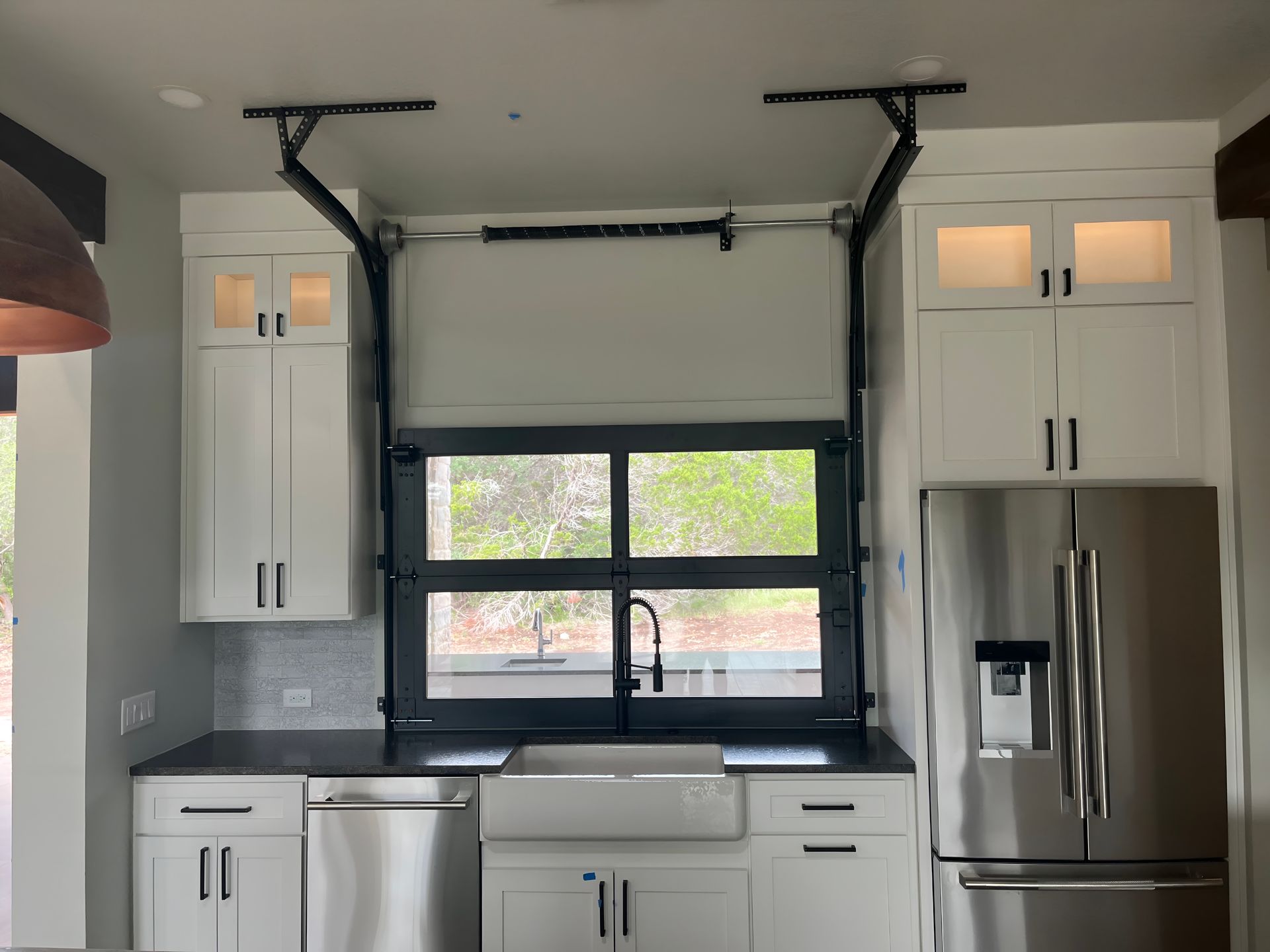 Modern kitchen with black-and-white cabinets, stainless steel fridge, sink, and large window with a roller shade