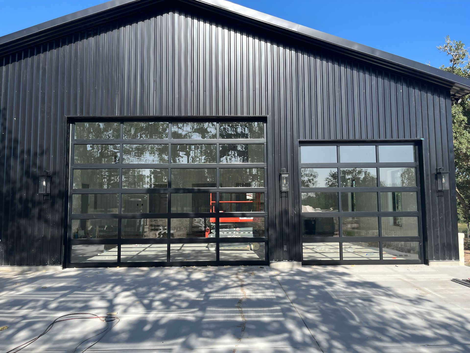 Black metal building with large glass garage doors and a concrete driveway in front.