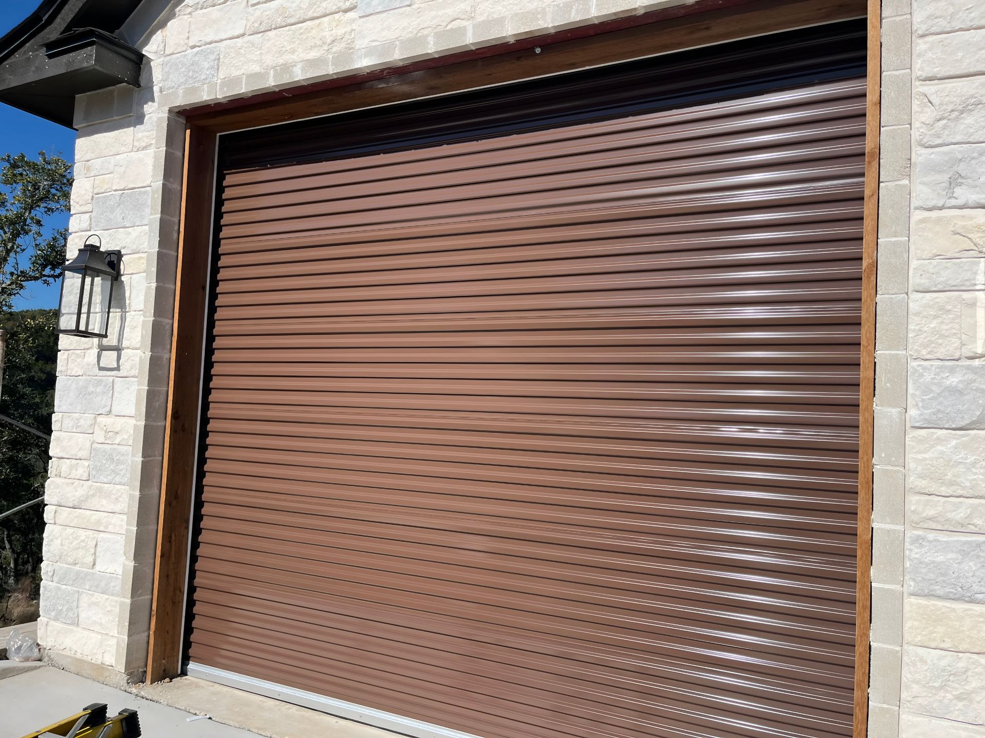 Closed brown metal roll-up garage door set in a stone wall in bright sunlight