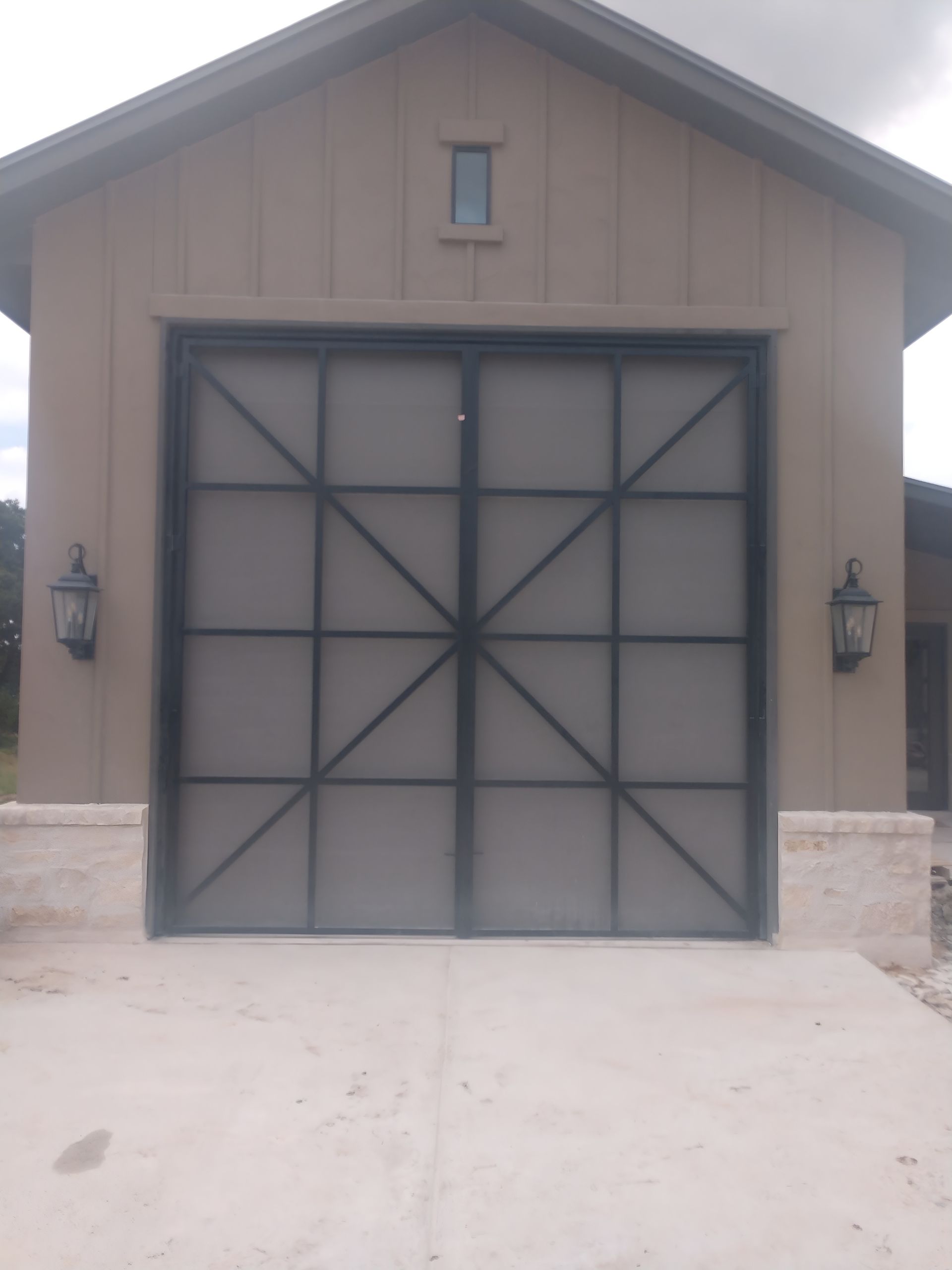 Front view of a tan garage with a large black double door and small window above it
