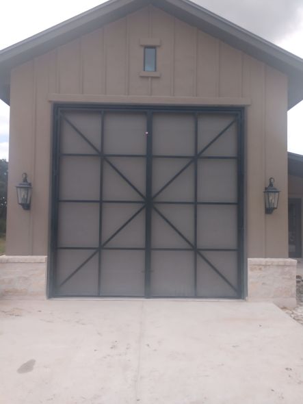 Front view of a tan garage with a large black double door and small window above it