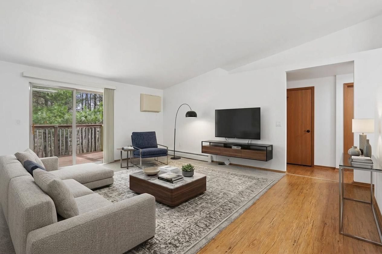 Bright living room with gray sofa, armchair, rug, coffee table, TV, and large window.