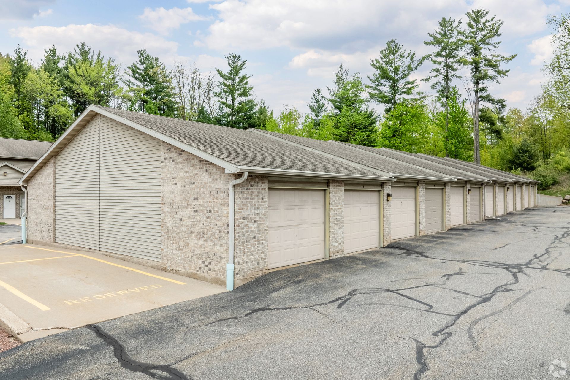 Row of beige garage units beside a cracked asphalt lot with trees in the background