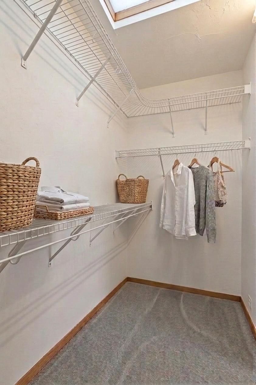 Small walk-in closet with wire shelving, hanging clothes, baskets, and a skylight above.