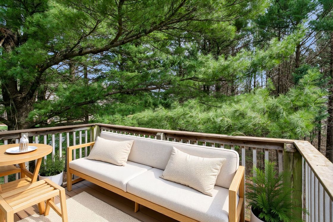 Wooden deck with cushioned bench and table overlooking lush green trees