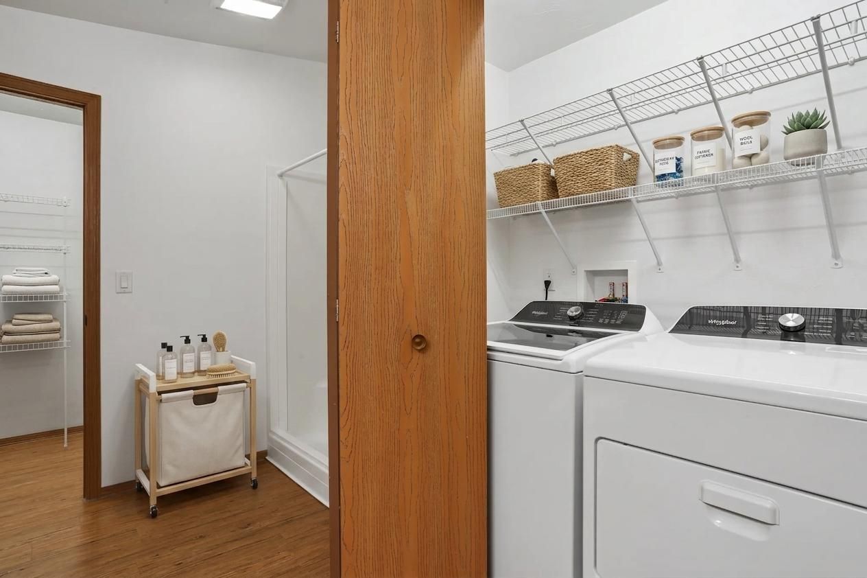 Laundry room with white washer and dryer, wooden door, and shelving with supplies