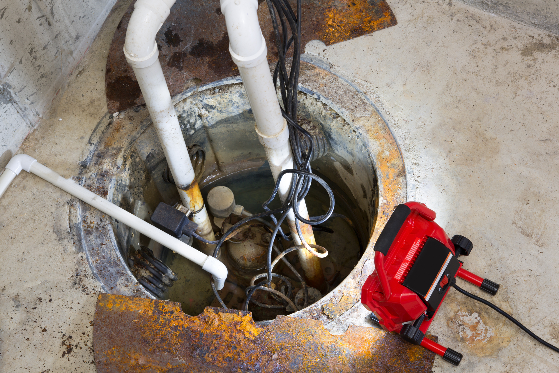 Dirocco plumbers repairing a sump pump in a basement with a red LED light illuminating the pit and pipe work for draining groundwater