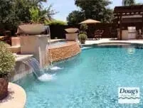 Resort pool with a small waterfall and lounge chairs under umbrellas