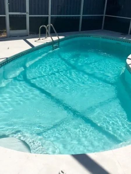 Sunny backyard swimming pool with clear blue water and a metal ladder by the deck
