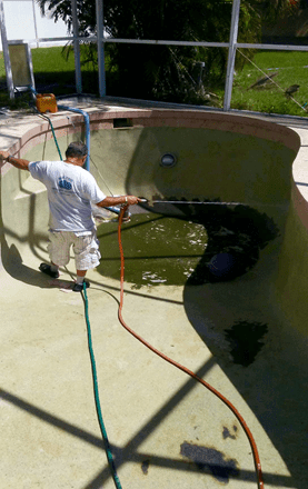 Person cleaning a drained pool with a hose and pressure washer, surrounded by a safety fence.