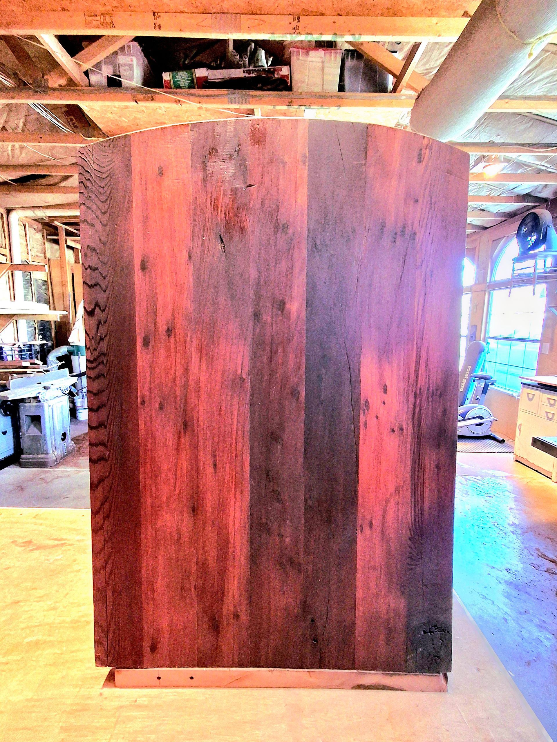 Large dark wooden panel standing upright in a rustic workshop with exposed beams and tools in the background