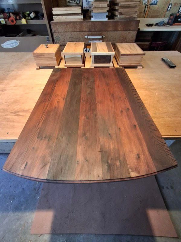Wooden tabletop boards laid out in a workshop, with cabinets and tools in the background.