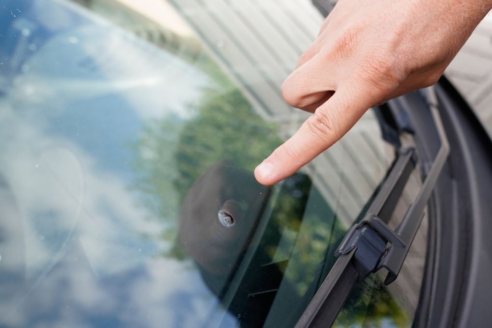 A Person is Pointing at a Hole in the Windshield of a Car — Crakka Windscreens in Diamond Beach, NSW