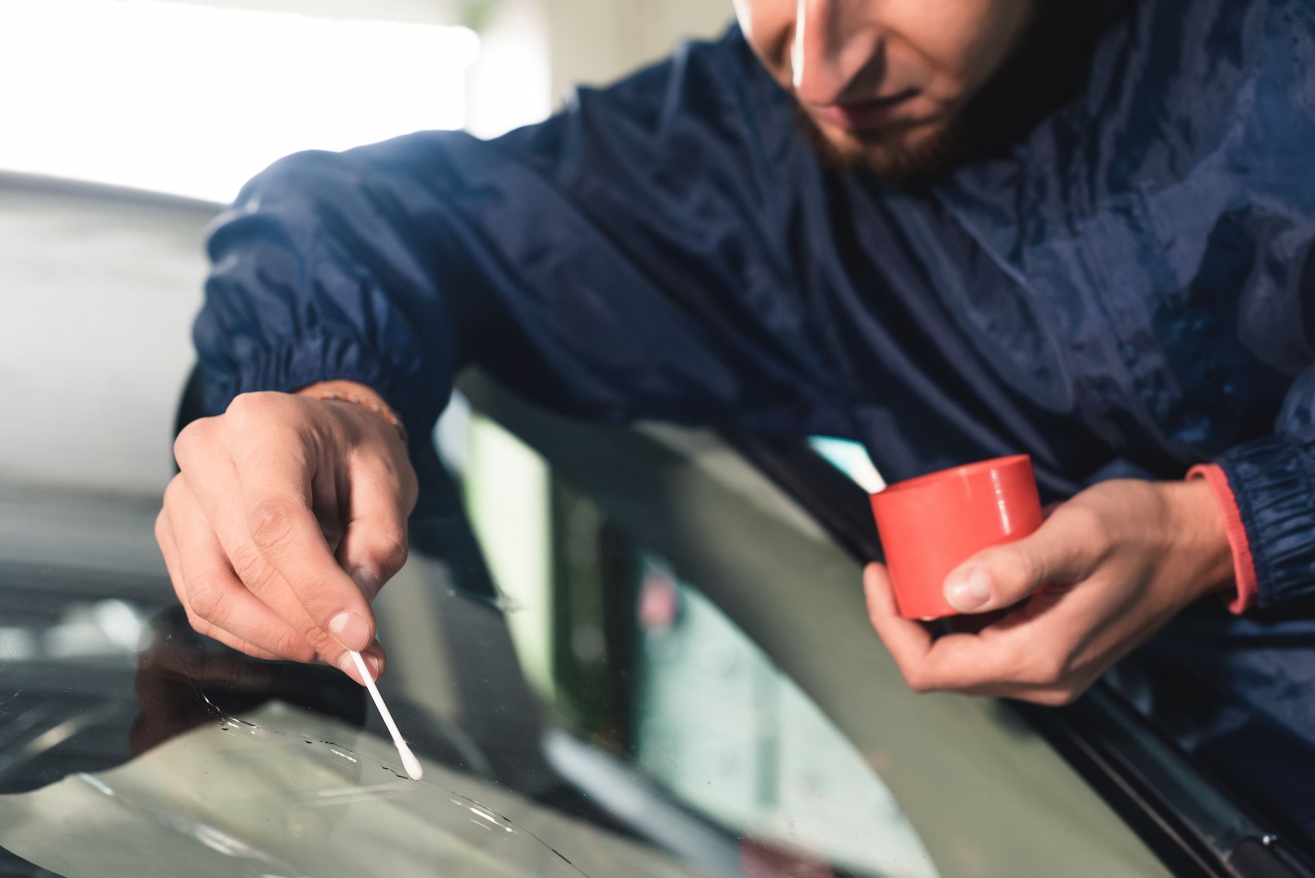 A Man is Cleaning a Windshield With a Cotton Swab — Crakka Windscreens in Diamond Beach, NSW