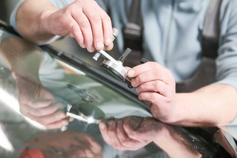 A Man is Fixing a Broken Windshield on a Car — Crakka Windscreens in Harrington, NSW
