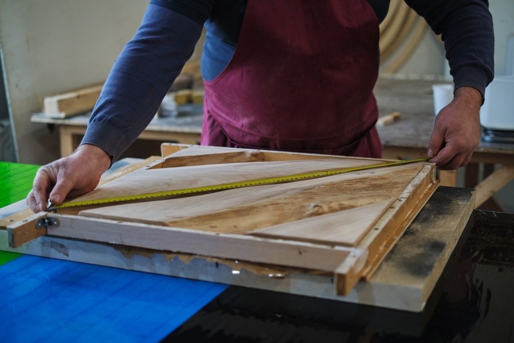 A Man Is Measuring A Piece Of Wood With A Tape Measure — ASM Joinery In Fyshwick, ACT