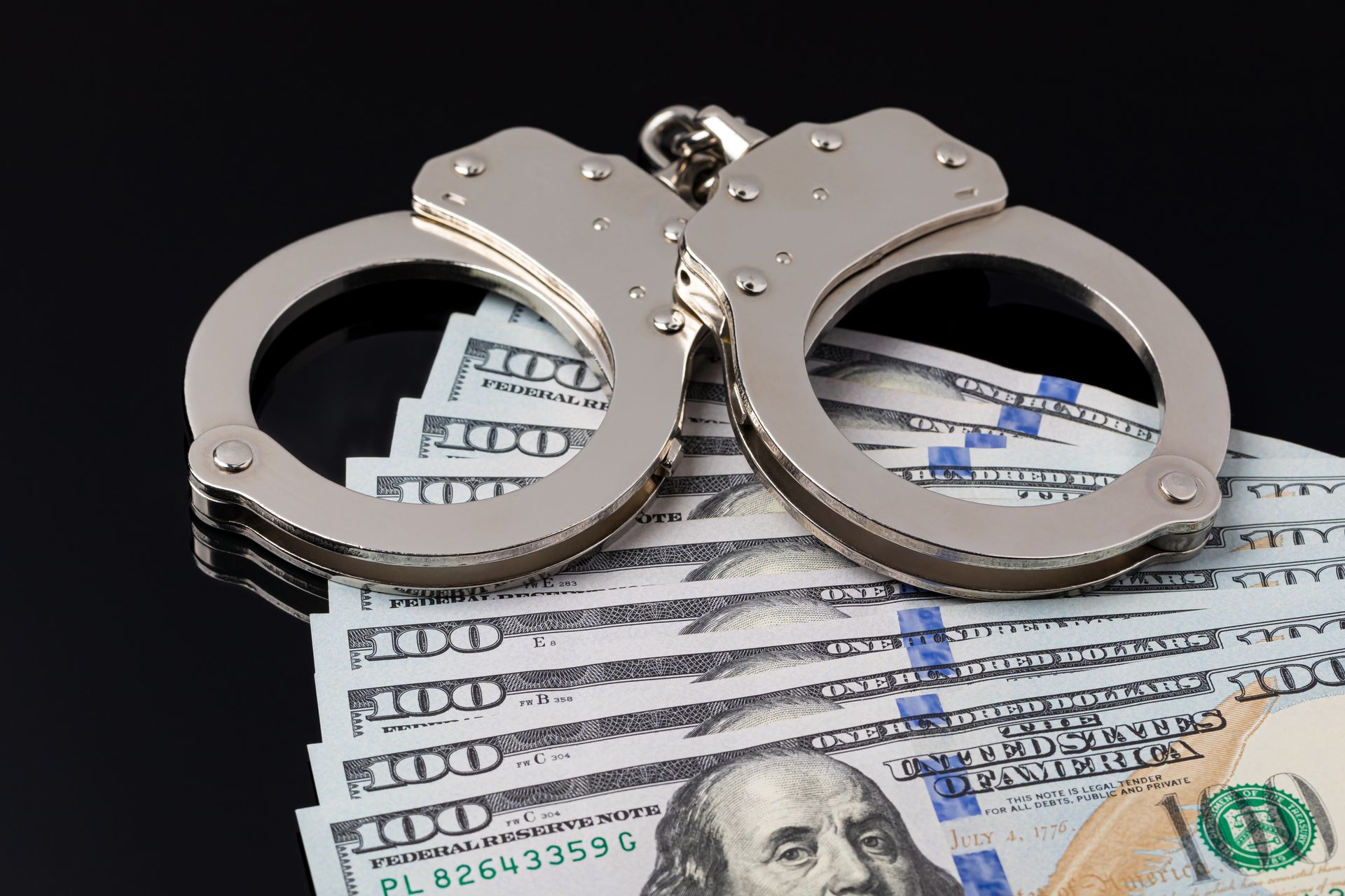 Handcuffs resting on U.S. dollar bills, symbolizing crime or financial arrest