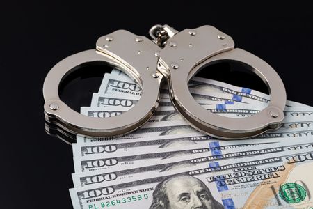 Handcuffs resting on U.S. dollar bills, symbolizing crime or financial arrest