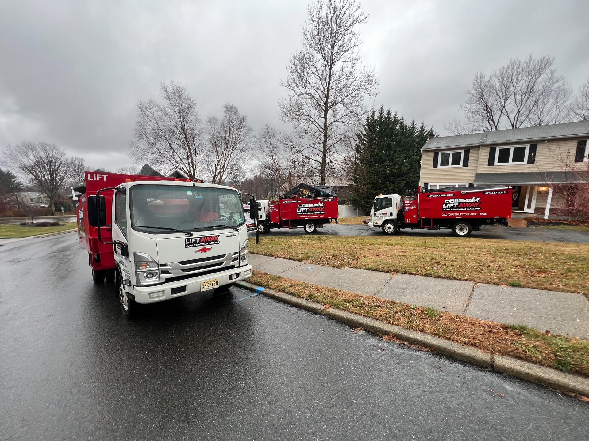 Three red and white tree service trucks parked on a street in front of a house on a cloudy day.
